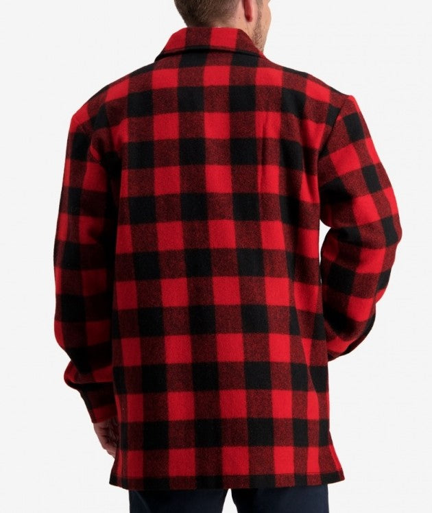 A person is standing with their back to the camera, wearing a Swanndri Longford Wool Shacket in a red and black checkered pattern. The shacket features long sleeves and is made of thick, warm 100% wool material with a lightweight twill lining. The background is plain white.
