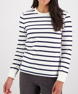 A woman wears the Swanndri Papamoa Stripe Long Sleeve Tee, featuring horizontal navy blue stripes and dark pants, standing against a plain light background.