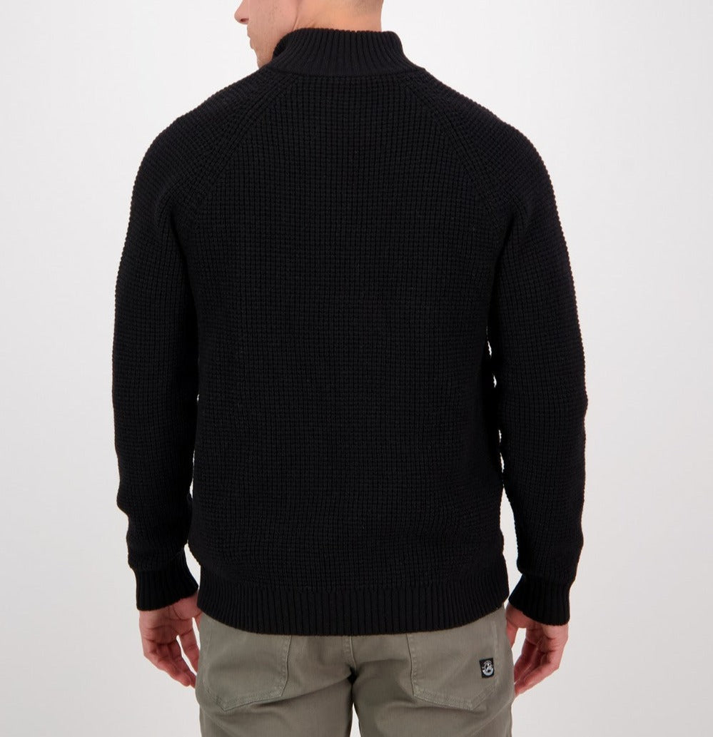 A man stands with his back to the camera, wearing the Swanndri Chalky Island Waffle Jumper in black and light gray pants against a plain white background.
