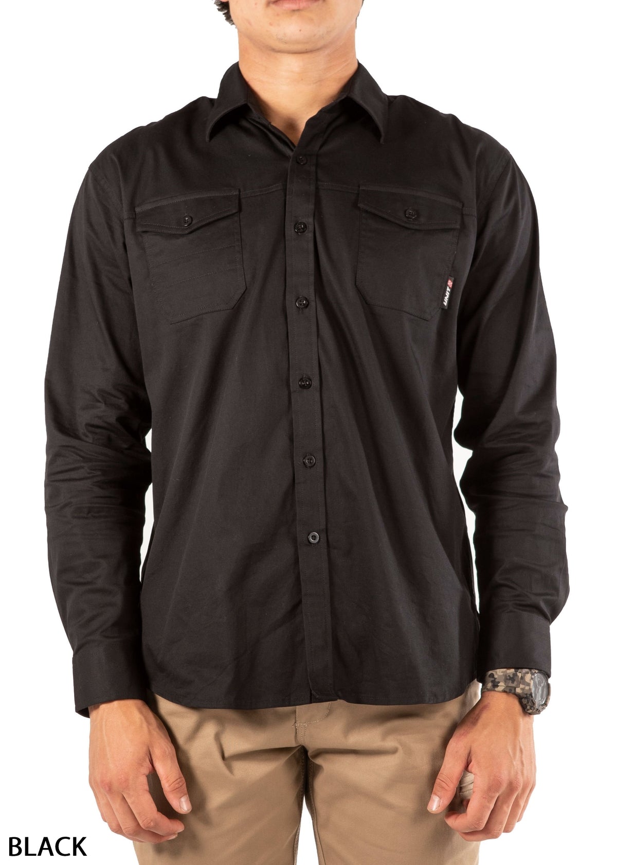 A man wearing the UNIT Craftman Stretch Shirt in black with two chest pockets and khaki pants stands against a white background. "BLACK" appears in the bottom left corner.