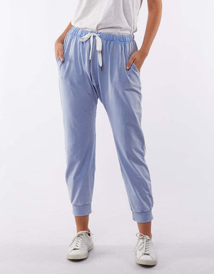 A person in a white t-shirt and light blue Foxwood Victoria Pant made of comfortable cotton fabric, featuring an elastic waist with a white drawstring, pockets, and elastic cuffs. The individual is wearing white sneakers and standing against a plain background.