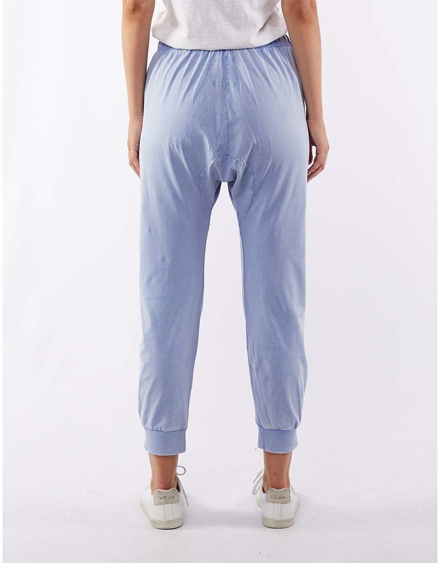 A person wearing a white shirt, Foxwood Victoria Pant in light blue with an elastic waist, and white sneakers stands facing away from the camera against a plain white background.