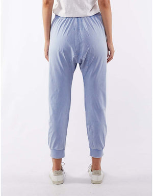 A person wearing a white shirt, Foxwood Victoria Pant in light blue with an elastic waist, and white sneakers stands facing away from the camera against a plain white background.