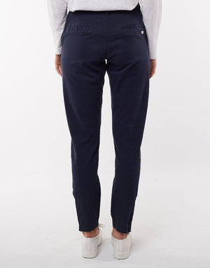A person wearing dark blue, comfortable Foxwood Liberty Pant and a light-colored long-sleeve top, seen from the back. The pants accentuate a relaxed style. The person is also wearing white sneakers against a plain white background.