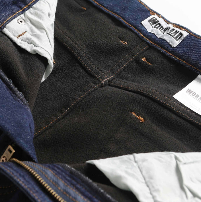 Close-up of the inside of a pair of Workland Polar Fleece Stretch Jeans showing the dark lining, orange stitching, and white pockets. A label with the text "WorldMap" is visible at the waist area. The stretch denim jeans are partially zipped open, displaying the metal zipper.