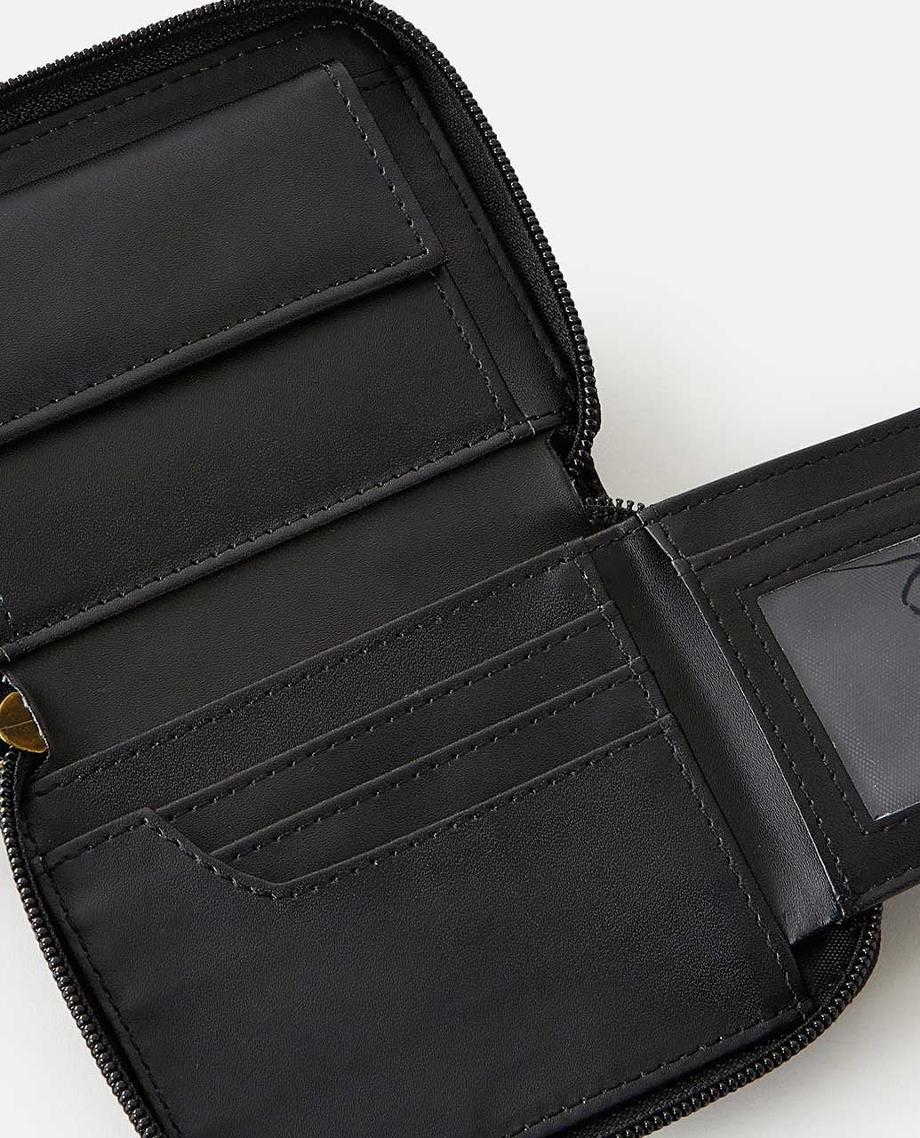 The Rip Curl Wanderer Small Zip Wallet is open, showcasing card slots, a clear ID window, and a coin zippered section. Designed with minimalism in mind, its neatly stitched interior emphasizes organization. The empty wallet's black leather stands out against a white background.