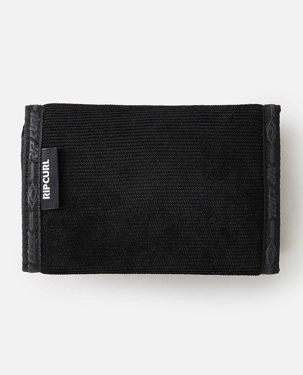 The Rip Curl Archive Cord Surf Wallet, shown closed against a white background, is a black fabric wallet with a small "Rip Curl" tag on the side. It features a simple and minimalist design with textured material and subtle patterned edges. The wallet includes a velcro closure and an ID window.