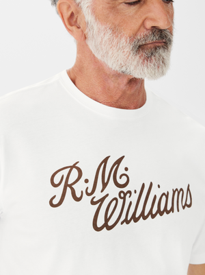 A person with a gray beard wears the RM Williams R.M.W Script T-Shirt, featuring brown cursive lettering on a regular fit cotton design, set against a plain white background.