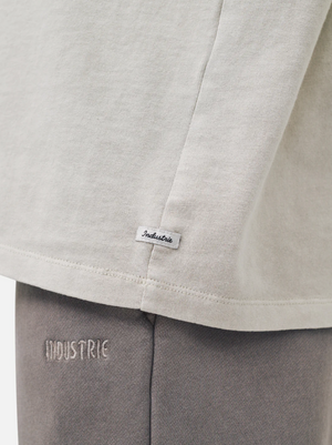 Close-up of the Industrie The Del Sur Tee in light beige, made from 100% cotton with an oversized fit. Features "INDUSTRIE" branding on a small shirt tag and detailed embroidery on gray pants, showcasing quality craftsmanship.