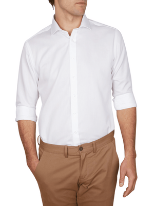 A man wears an Abelard Non Iron Cotton Twill Slim Fit Shirt with a cutaway collar. The crisp white shirt, untucked over tan pants, is styled with rolled-up sleeves as he rests his left hand in his pocket against a plain white backdrop.