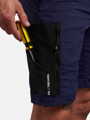 A person is seen wearing King Gee Trademark Cargo Shorts in dark blue, featuring a black zipper pocket with white text. The durable and flexible stretch ripstop fabric of the shorts holds a yellow screwdriver partially inserted into the stylish side pocket.