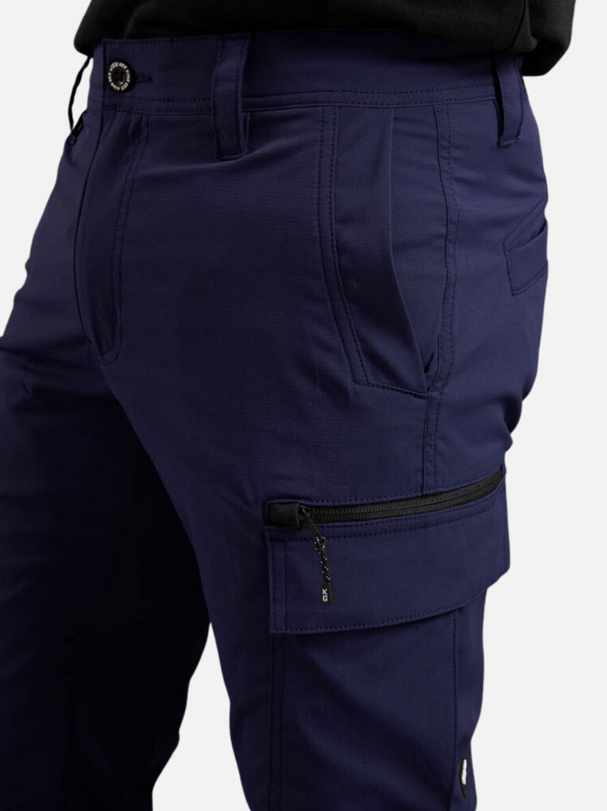 A person wearing King Gee Trademark Cargo Pant in dark blue with a side zipper pocket stands against a white background. The pants feature durable ripstop fabric, belt loops, and a button closure.