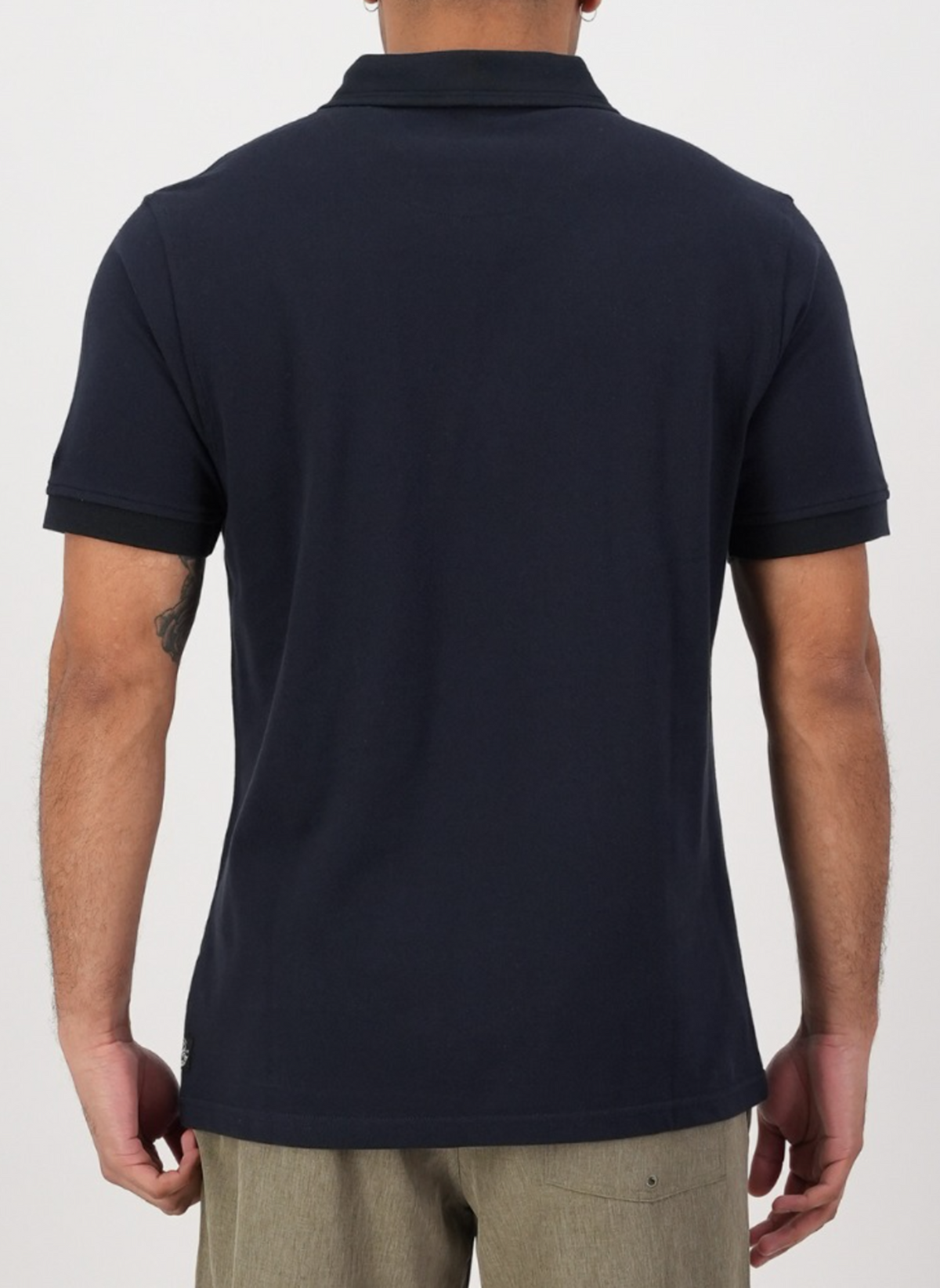 A person is shown from the back wearing a navy Swanndri Highgrove Polo made of 100% combed cotton and light gray pants, set against a plain white background.