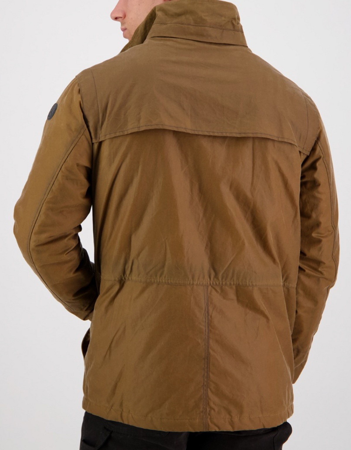A man is seen from the back wearing a Swanndri Evans Flat Oilskin Jacket in brown with a high collar, black sleeve patch, visible stitching, and cozy quilted lining. The background is plain white.