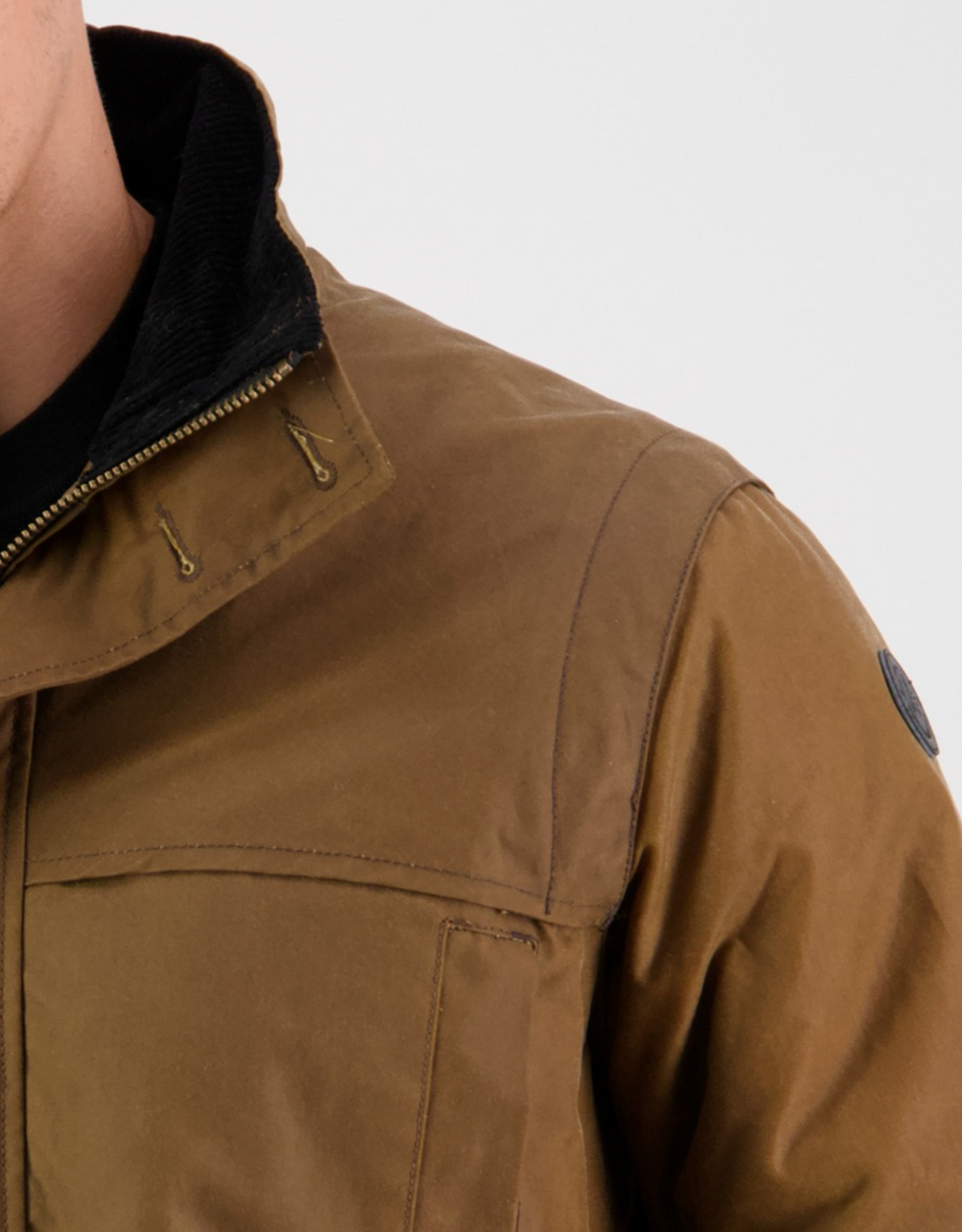 Close-up of someone wearing the Swanndri Evans Flat Oilskin Jacket, featuring a black collar, zipper details, quilted lining, shoulder patch, and visible stitching against a neutral backdrop.