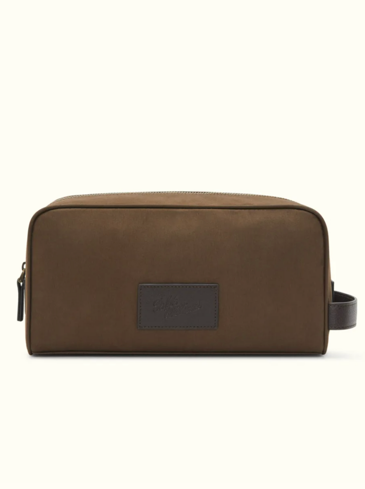 The RM Williams Hawkesbury Washbag is a brown, rectangular waxed cotton travel bag with a top zipper, side handle, dark brown patch with embossed text, and waterproof lining. Shown on an off-white background.