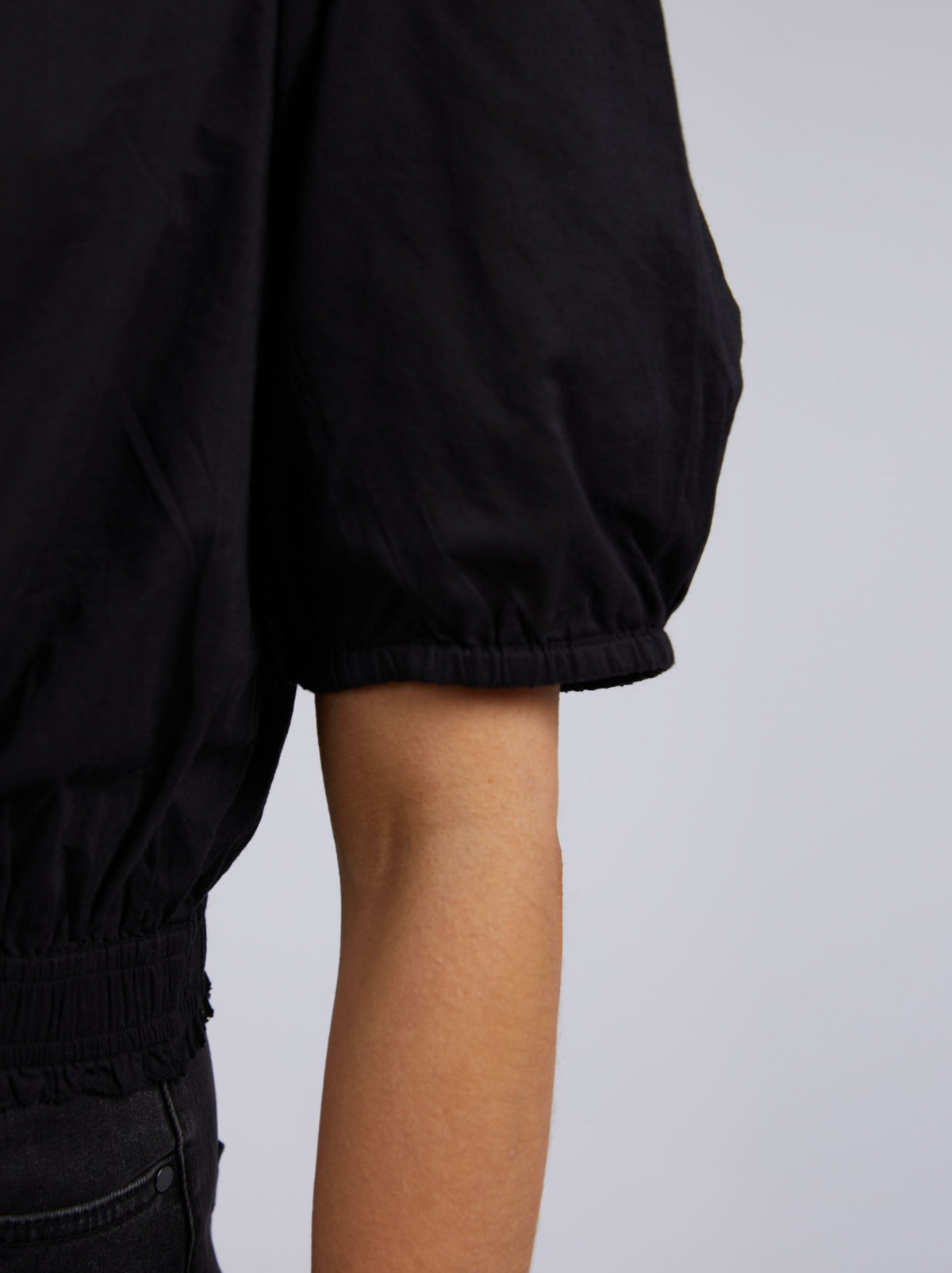Close-up of someone wearing the Foxwood Charli Top—black with puff sleeves and a chic cropped fit. The image highlights the arm and gathered sleeve detail against a plain, light backdrop.