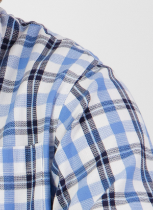 Close-up of the Swanndri Russell Shirt in blue, black, and white plaid with a front pocket. Made from 100% cotton for a relaxed fit, shown against a light background featuring part of the wearer's shoulder and chest.