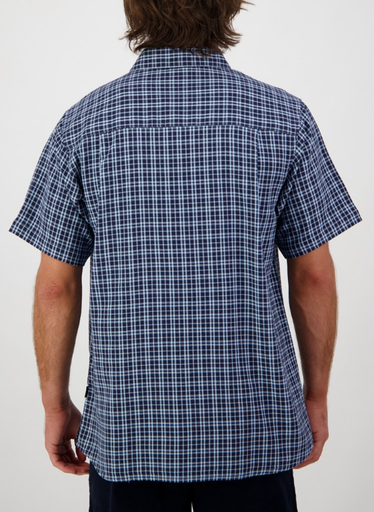 A person with medium-length brown hair is seen from behind, wearing the Swanndri Russell Shirt in blue and white checks, made of 100% cotton with a relaxed fit. The background is plain white.