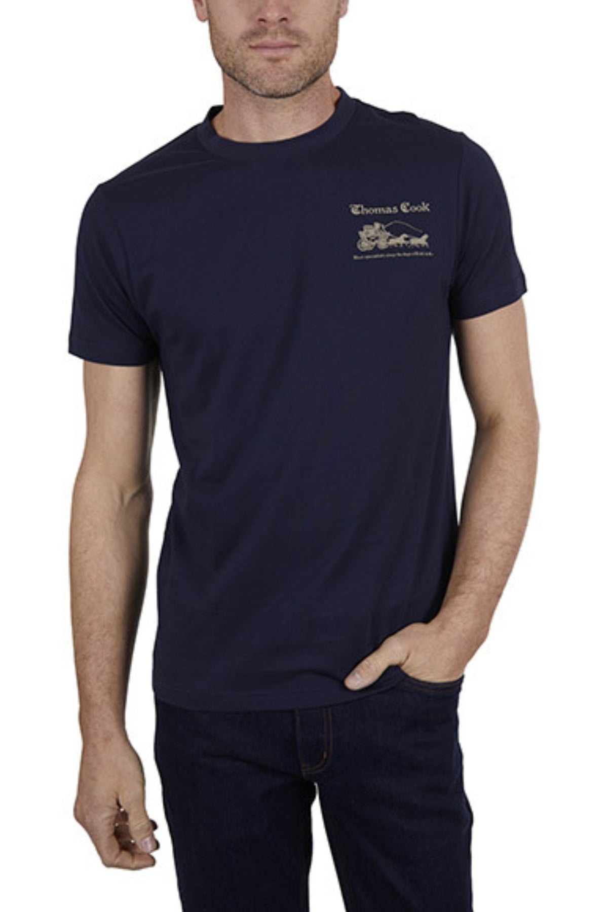 A man wears the Thomas Cook Coach Tee, a lightweight cotton jersey featuring a small logo and illustration on the left chest, paired with dark jeans and standing with one hand in his pocket.