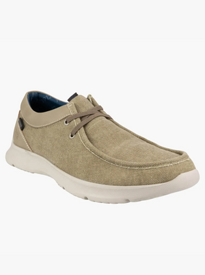 The Florsheim Bushwacker Canvas Slip-On features a casual beige canvas design with brown laces and a white rubber sole, displayed diagonally on a plain background. It has a dark blue interior lining and memory foam insole for added comfort.