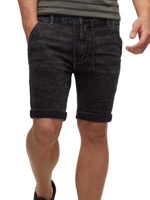 A person models Industrie The Drifter Denim Short in black—skinny fit with rolled-up hems and a drawstring waist. Only the lower torso and legs are shown, hands resting near the pockets—ideal for summer style.