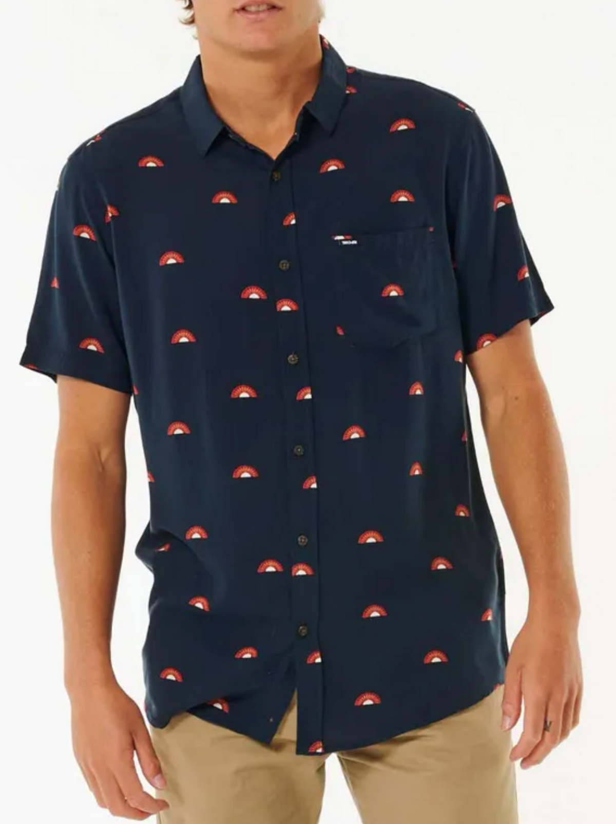 A person wearing the Rip Curl Party Pack Short Sleeve Shirt, which is navy with a red and white semi-circle pattern and has a comfortable fit, paired with tan pants and standing against a plain white background.