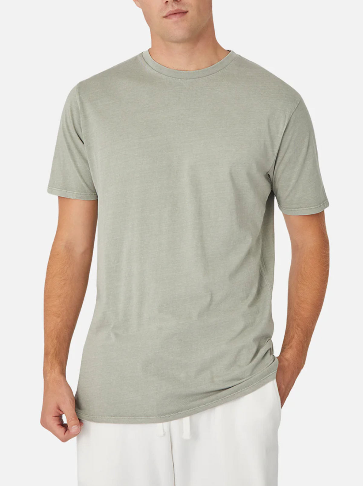 A person stands against a white background wearing the Industrie The Basic Classic Tee in gray, made of 100% cotton, featuring a timeless loose fit. They pair it with white pants and face slightly left, with their left hand partially in their pocket.