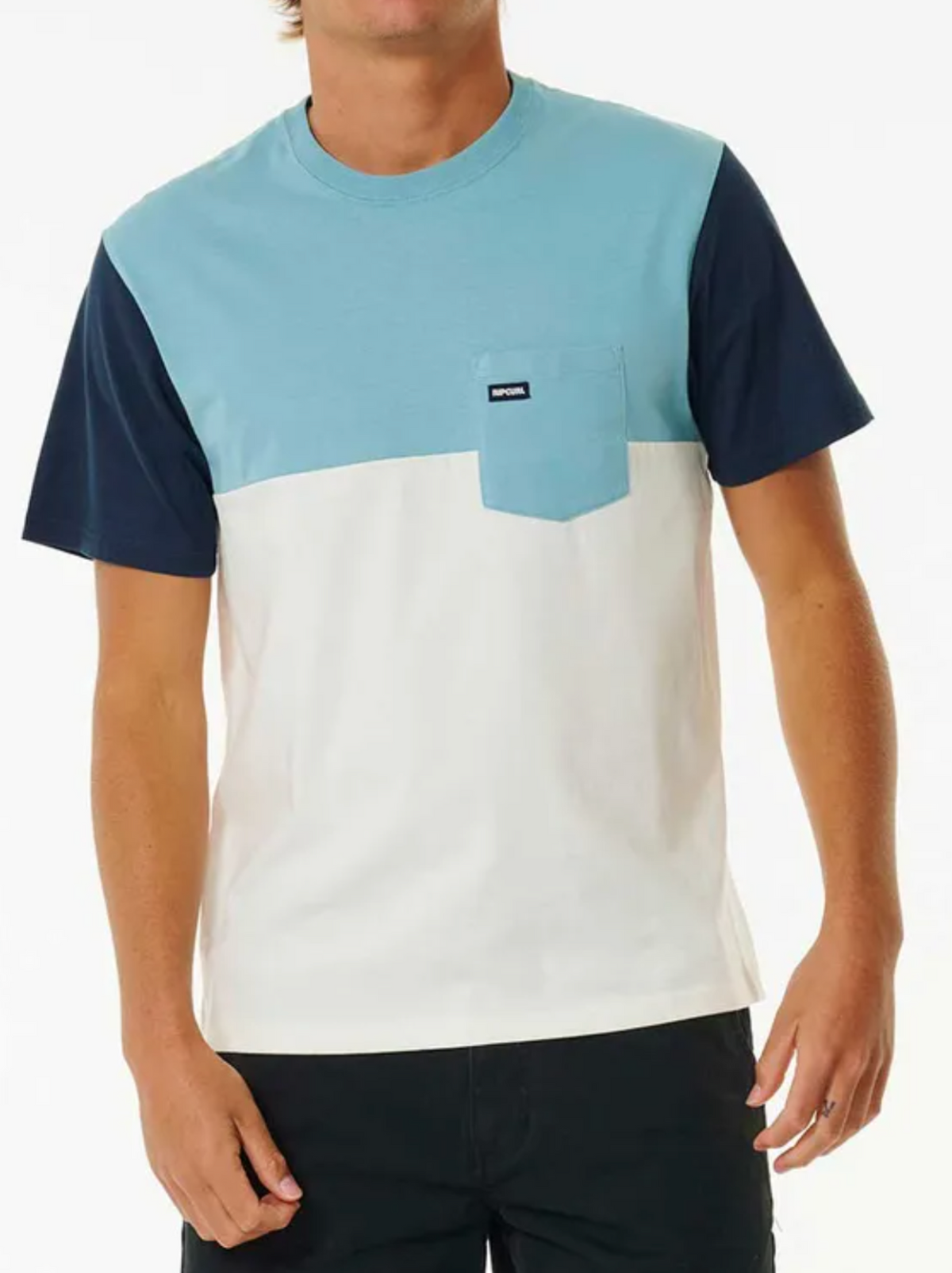 A man wears the Rip Curl Surf Revival Custom Tee, featuring blue sleeves, a light blue chest with a pocket, and a white lower half made from 100% cotton. This stylish tee pairs well with his dark shorts. The image is cropped above his eyes.