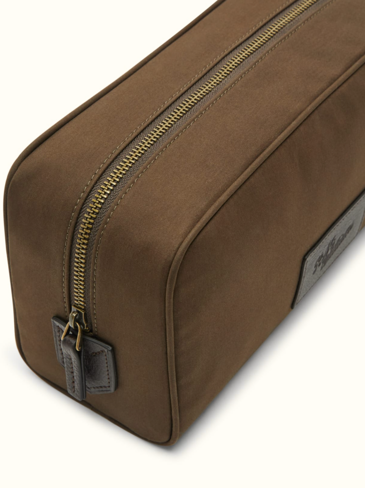 A close-up of the RM Williams Hawkesbury Washbag, a brown rectangular travel bag made from waxed cotton with a gold zipper and leather pull tab, displayed on a light background.