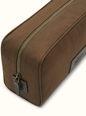 A close-up of the RM Williams Hawkesbury Washbag, a brown rectangular travel bag made from waxed cotton with a gold zipper and leather pull tab, displayed on a light background.