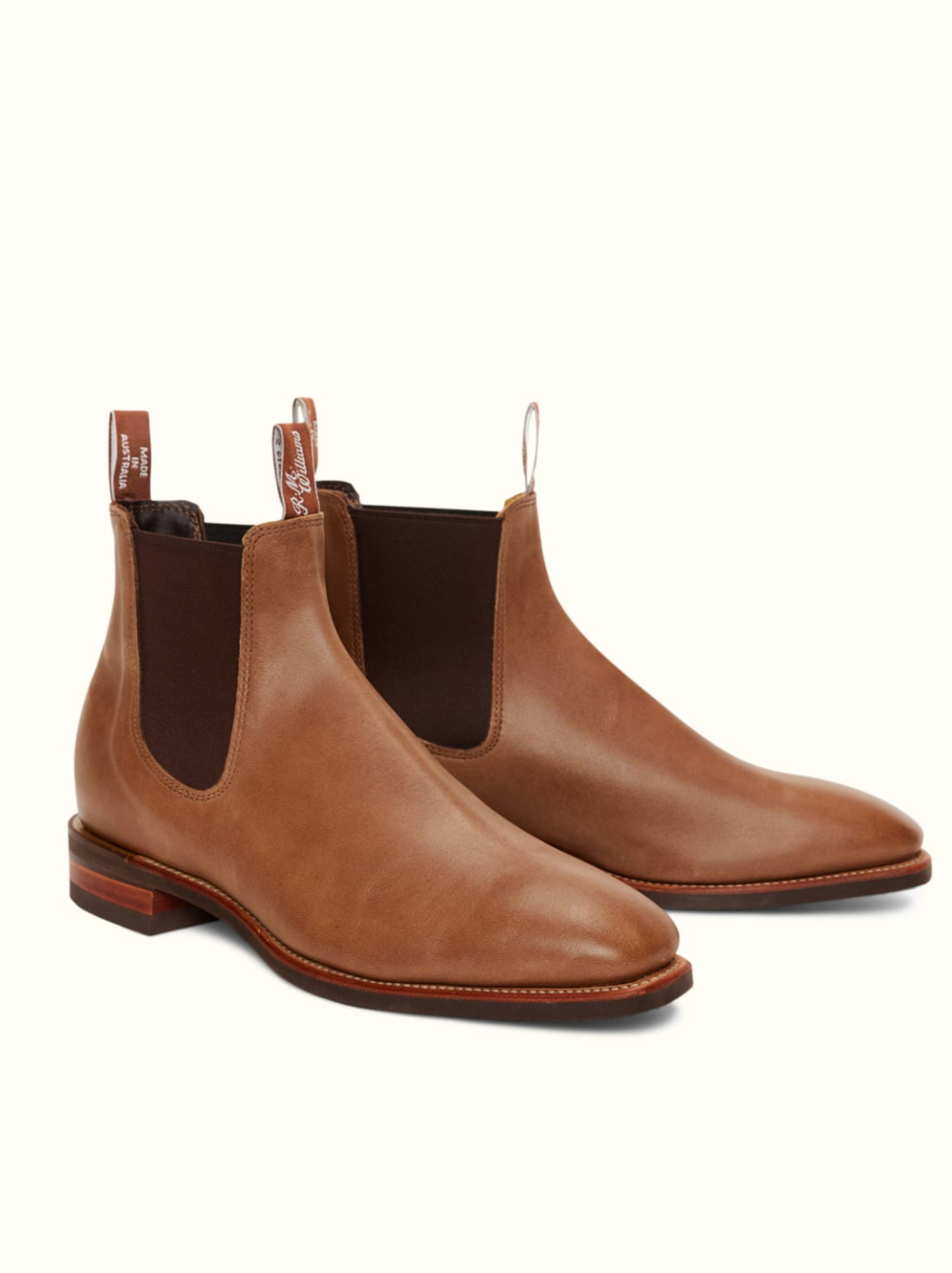 The RM Williams Comfort Craftsman Boot is a pair of brown leather Chelsea boots featuring elastic side panels and pull tabs at both the back and front. These boots have a chisel square toe, a slight heel, and a smooth, polished finish. They are displayed against a plain, light background.