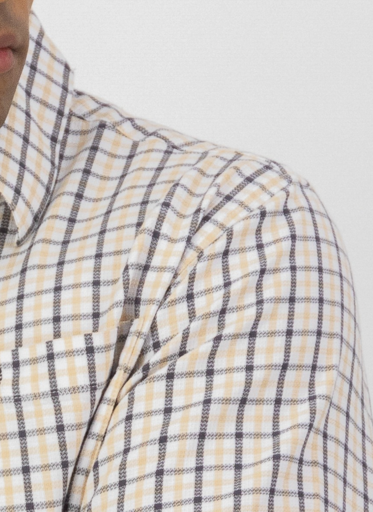 Close-up of a person wearing the Swanndri Russell Shirt, shown from the shoulders up against a plain white background. The shirt features a yellow and black checkered pattern, relaxed fit, and is made from 100% cotton. Face partially visible on the left.
