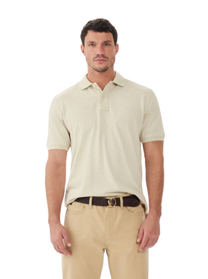 A man wears an RM Williams Rod Polo in light beige, made from breathable cotton pique, paired with khaki pants and a dark brown belt, standing against a plain white background.