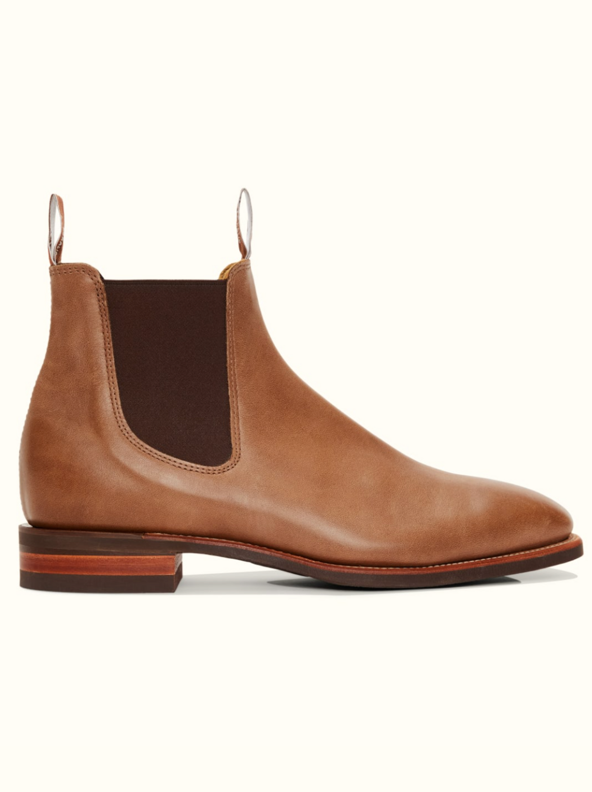 A single RM Williams Comfort Craftsman Boot in tan leather with a chisel square toe, featuring a brown elastic side panel, a pull tab at the back, and a wooden sole with a low heel, viewed from the side on a plain white background.