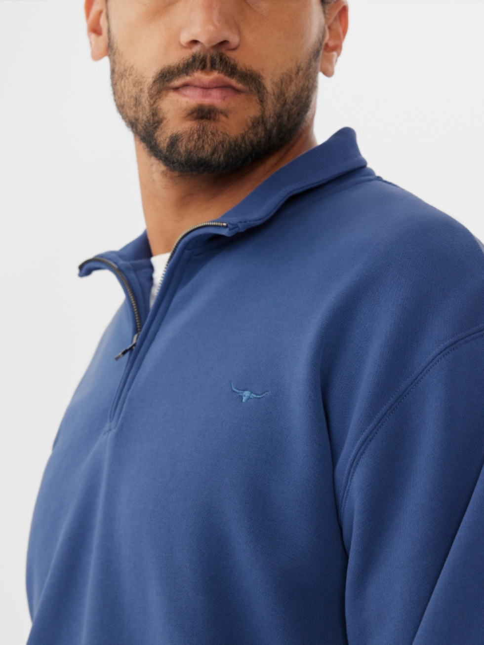 A man wearing the RM Williams Mulyungarie Fleece, a blue vintage-inspired quarter-zip pullover with a small chest logo, against a plain white background.