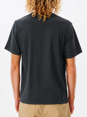 A person with curly, shoulder-length hair is seen from behind, wearing a relaxed fit black Rip Curl Plain Wash Tee and light brown shorts against a white background.