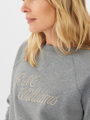 A blonde woman is wearing the RM Williams R.M.W Womens Script Crew, a gray sweatshirt with classic design. The side profile photo captures her head and upper torso against a white background, emphasizing her functional style.