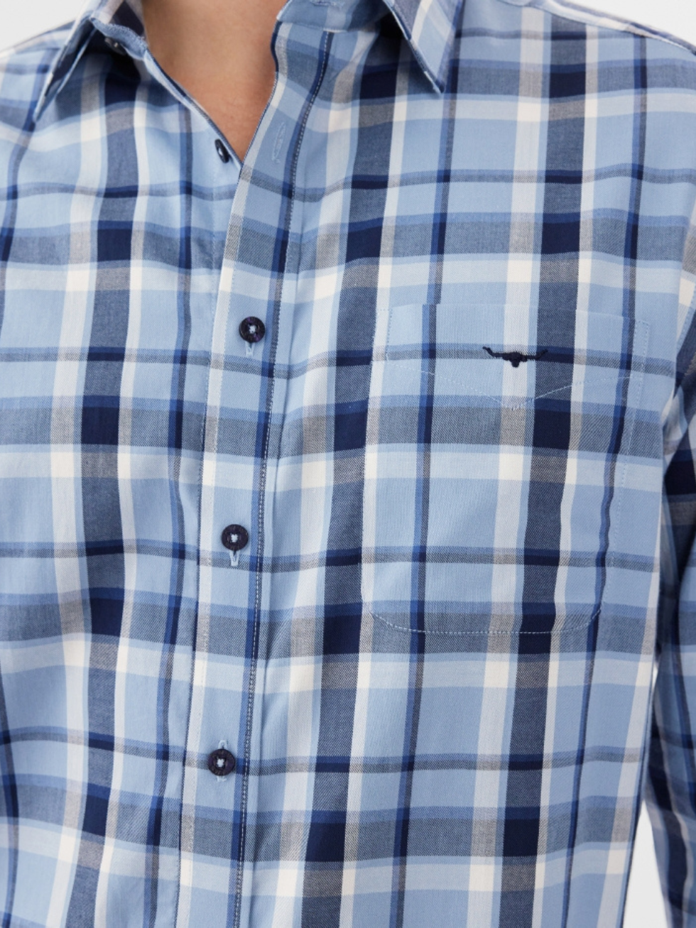 A close-up shows a person wearing the RM Williams Collins Shirt in blue and white plaid. The lightweight cotton twill fabric includes front buttons, a chest pocket, and adjustable cuffs, featuring shades of light and dark blue with crisp white stripes.
