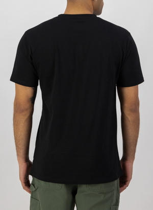 Rear view of a person wearing a Swanndri Original v2 Print T-Shirt in plain black, paired with olive green pants, standing against a light gray background. The individual has short hair and relaxed arms by their sides.
