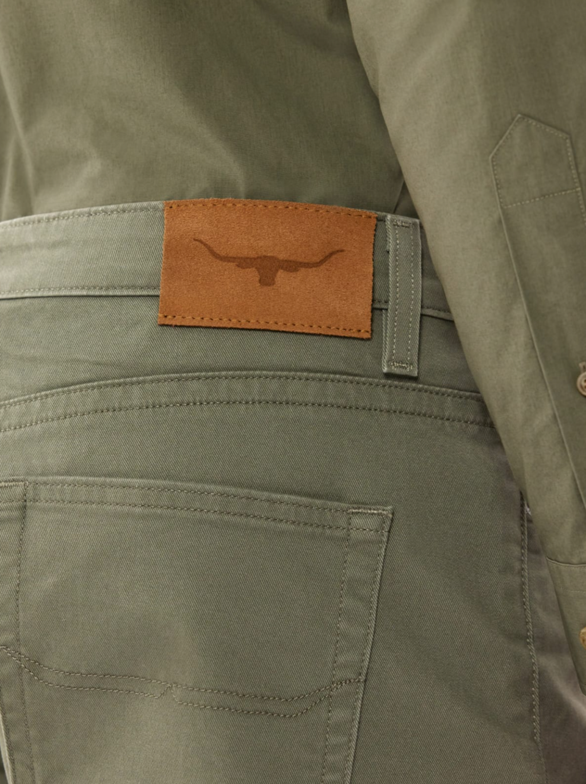 A person is wearing RM Williams Nicholson Shorts made from premium stretch cotton in gray, with a brown leather patch and bull's head logo on the back pocket, paired with a matching gray jacket for a smart casual look.