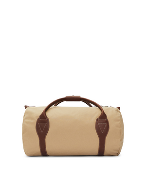 The RM Williams Sorrento Ute Bag showcases a beige duffel design complemented by brown leather handles and straps. Constructed from water-repellent utility canvas, this cylindrical-shaped bag stands upright with centrally positioned top handles. White-stitched leather accents and a partially visible zipper provide intricate detailing.