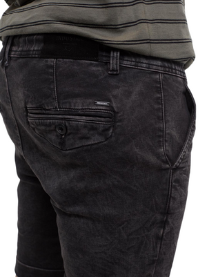 Close-up of a person wearing the Industrie The Drifter Denim Short in faded black, featuring a buttoned back pocket, paired with a striped green and gray shirt—ideal for relaxed summer style.