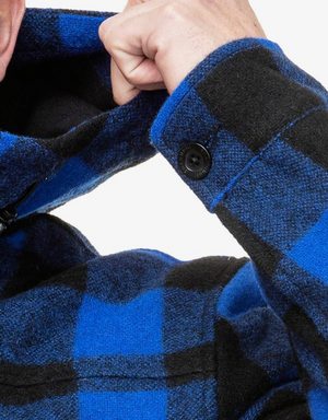 Close-up of a person adjusting the collar of a blue and black plaid Swanndri Hudson Hoody. The cuff, featuring a black button, hints at its detailed craftsmanship. The person’s face is not fully visible, focusing on the hand and fabric details of this premium New Zealand wool hoody.