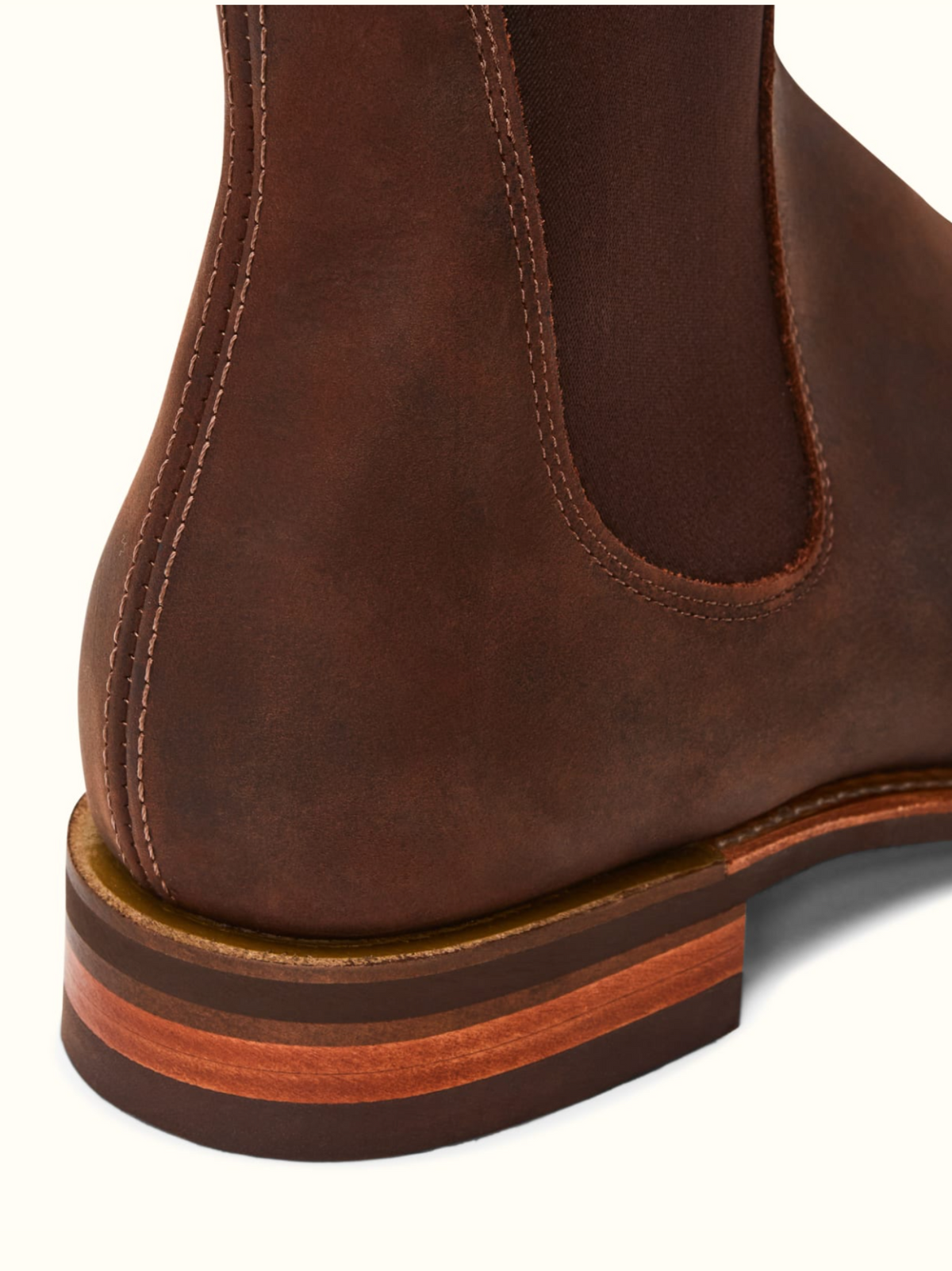 Close-up of the heel and lower side of a brown RM Williams Comfort Craftsman Boot, highlighting intricate stitching and a multi-toned stacked wooden sole.