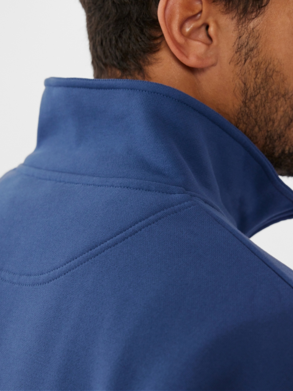 A person is seen wearing the RM Williams Mulyungarie Fleece, a vintage-inspired blue jacket with a high collar. The image focuses on the brushed cotton texture and rich color while highlighting the back and side of the person's head and shoulder.