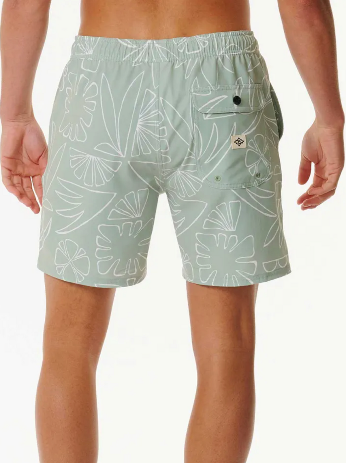 A person is seen from the back wearing Rip Curl SWC Plantation Volley shorts in light green with a white abstract floral pattern. The shorts feature an elastic waistband for comfort, quick dry fabric, and a back pocket with a stitched logo for added practicality.