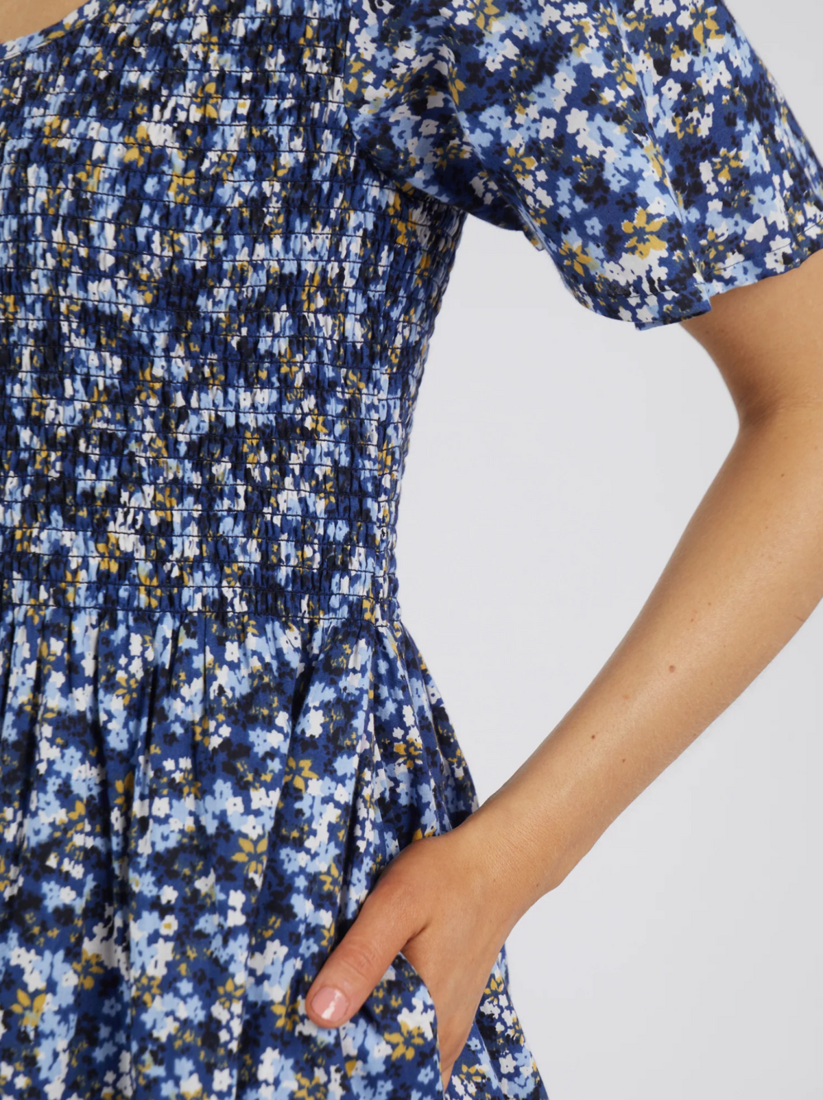 A close-up of a person wearing the Foxwood Lulu Dress in sapphire ditsy print, made from fresh cotton poplin with a gathered ruched bodice and their right hand casually placed in a pocket.