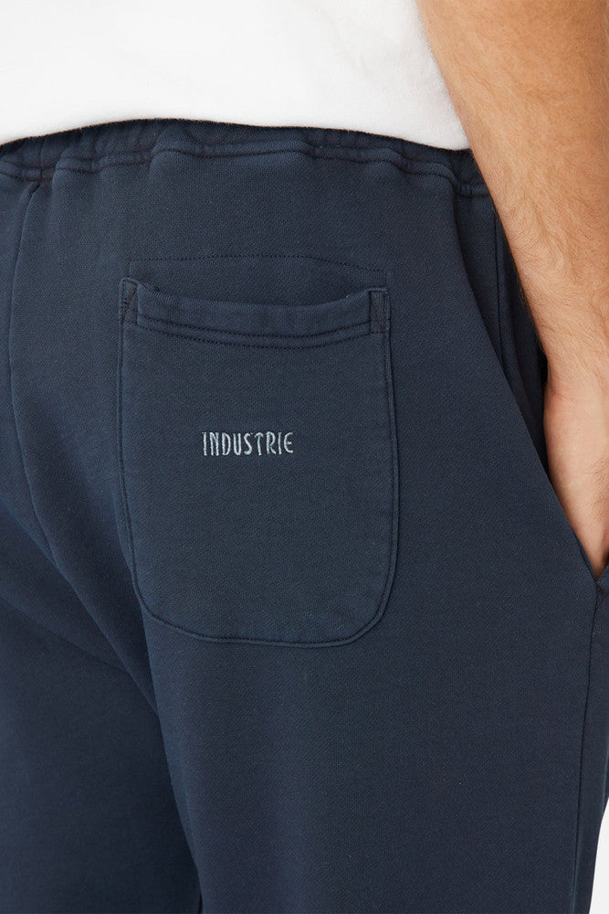 A person wears the Industrie The Del Sur Track Pant in navy, showcasing an embroidered white logo on the back pocket. Their hand is partially visible, casually tucked into the pocket.