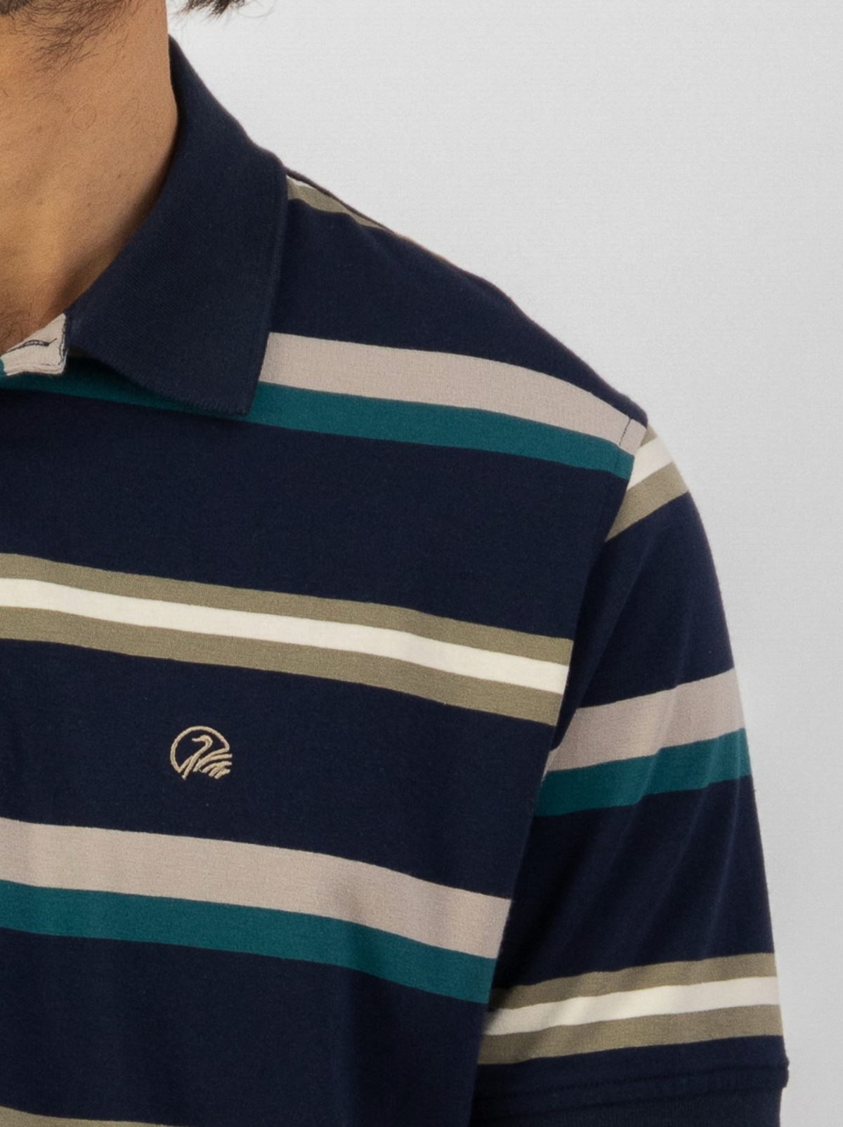 Close-up of a person in the Swanndri Winfred Stripe Polo, featuring comfortable cotton-elastane fabric, teal, beige, and light gray horizontal stripes, and an embroidered logo. Face not visible.
